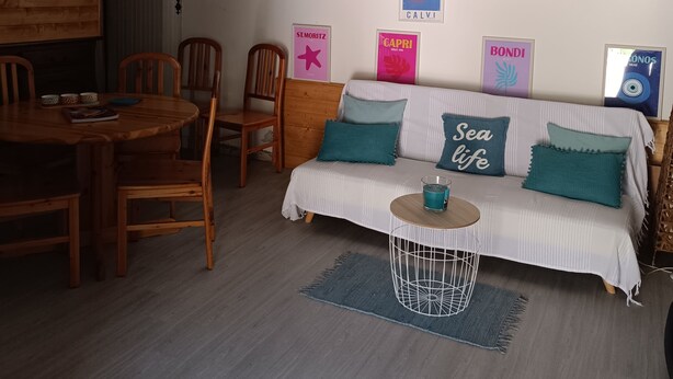 A cozy living room with a wooden dining table, chairs, a sofa with teal cushions, and a small side table with a candle. - 🌿Village house full of charm🌿 Haven of peace 5 minutes from a river 🌿 (Manso)