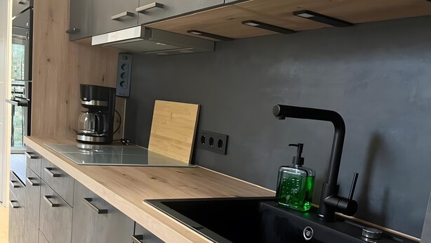 Una cucina moderna con lavello nero, piano di lavoro in legno e mobili grigi.