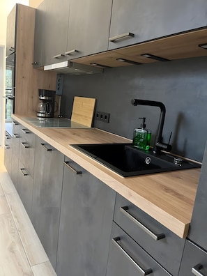 A modern kitchen with a black sink, wooden countertop, and grey cabinets.