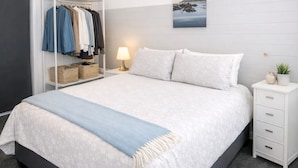 Een slaapkamer met een bed, een kledingkast, een nachtkastje, een lamp en een foto aan de muur.