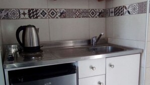 Eine kleine Küche mit Geschirrspüler, Spüle und einem Holzbodenregal darüber.