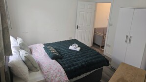 Un dormitorio con cama, almohadas, una colcha, un armario y una puerta que da a otra habitación.