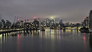 Un horizonte urbano nocturno con edificios iluminados reflejándose en el agua.
