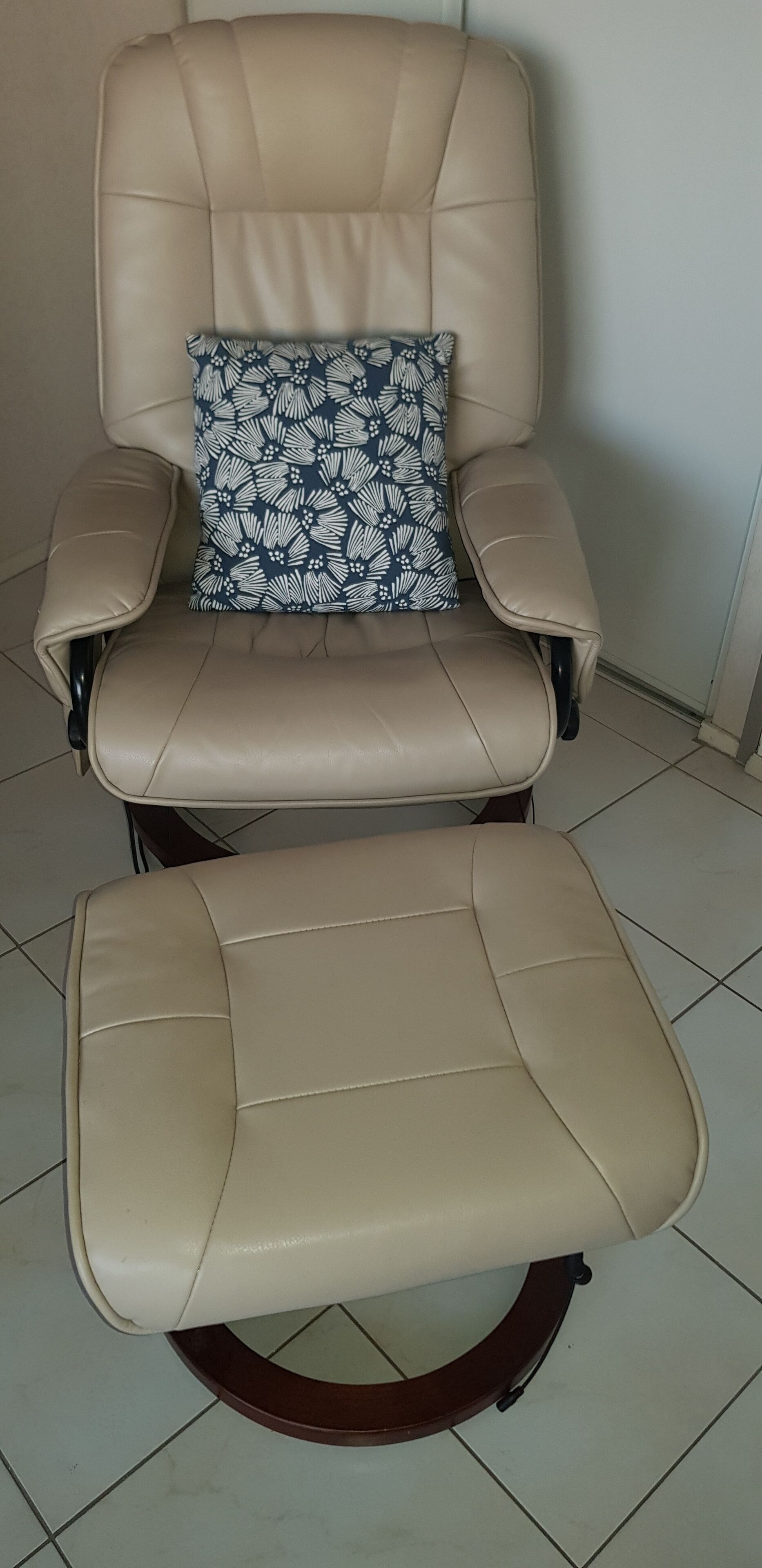 A beige leather recliner with a footrest and a matching cushion.