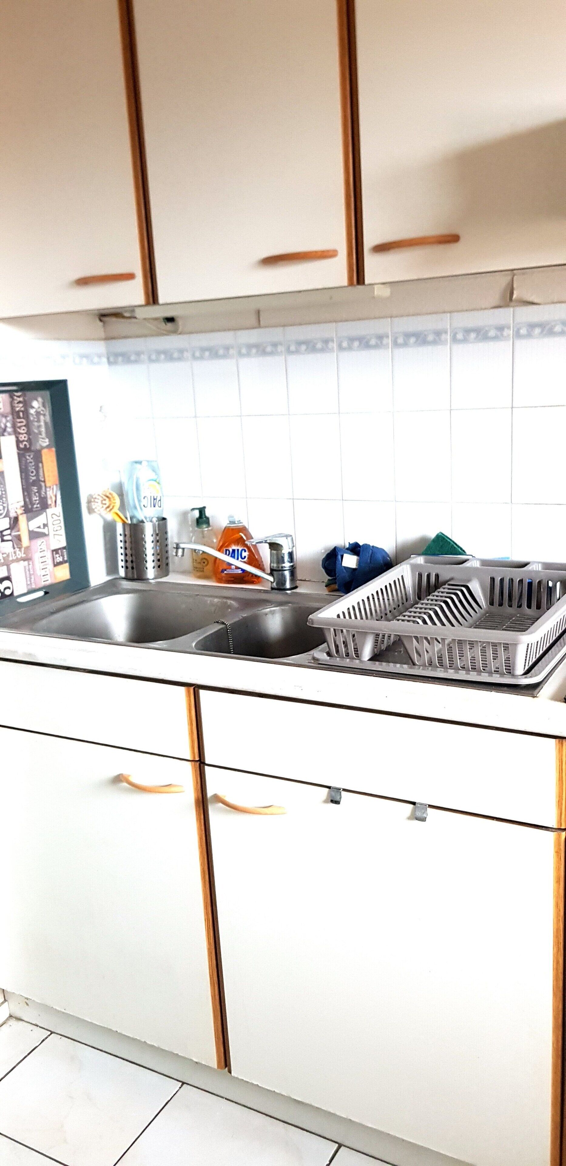 A kitchen with white cabinets, a stainless steel sink, and various kitchen items like a dish rack, a blue cloth, and a bottle of dish soap.