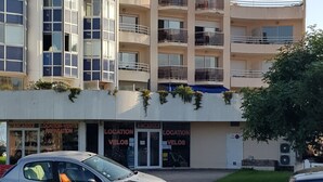 A multi-story building with a curved facade and balconies. A car is parked in front, and there are flower beds in the foreground. - T2 exceptional marina view (Arcachon)