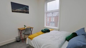 Ein Schlafzimmer mit Bett, Schreibtisch, Stuhl, Fenster und einem Bild an der Wand.