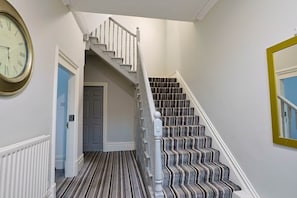 A staircase with a striped carpet and white balusters, leading to a door.