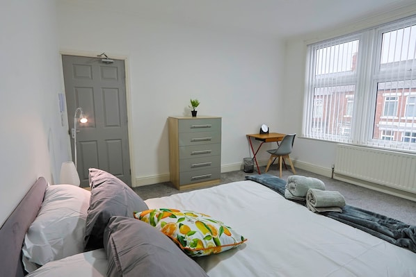 A bedroom with a bed, a desk, a chair, a wardrobe, and a window.