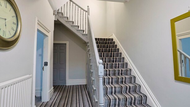 Un escalier recouvert d’une moquette à rayures et doté de balustrades blanches, menant à une porte.