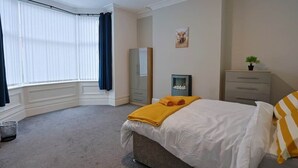 Une chambre à coucher avec un lit, une commode, un miroir et une fenêtre avec des rideaux.