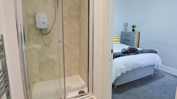 A modern bathroom with a glass-enclosed shower, a marble-tiled wall, and a visible towel rack.
