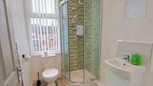 A bathroom with a toilet, a glass-enclosed shower, a sink, and a window.