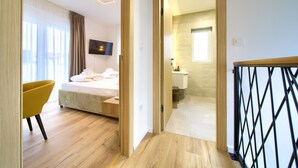 Een moderne hotelkamer met een bed, een gele stoel en een zichtbare badkamer door een open deur.