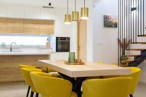 A modern kitchen with wooden cabinets, a central island, and a dining area with yellow chairs and a wooden table.