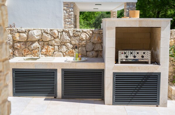 Une cuisine extérieure avec des murs en pierre, un barbecue encastré et des grilles de ventilation.