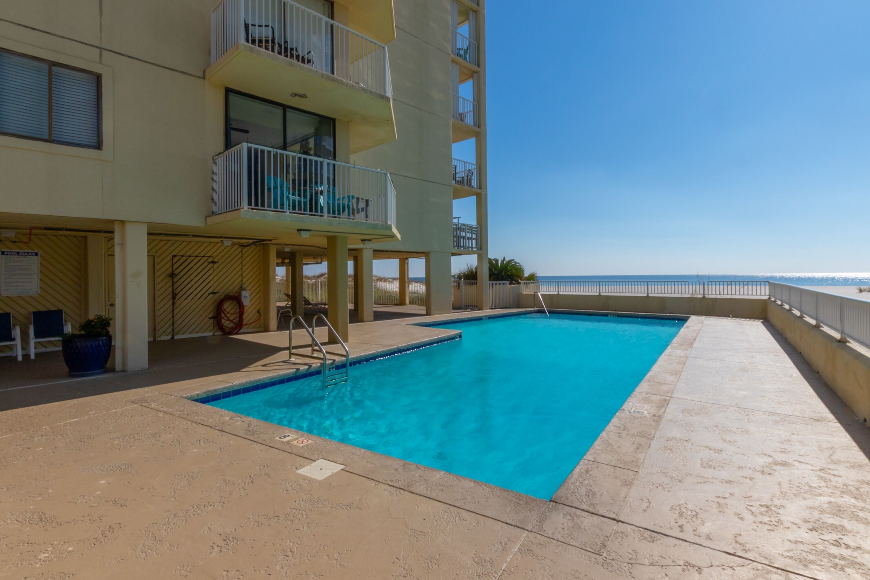 A swimming pool with a view of the ocean, a building with balconies, and a clear sky.