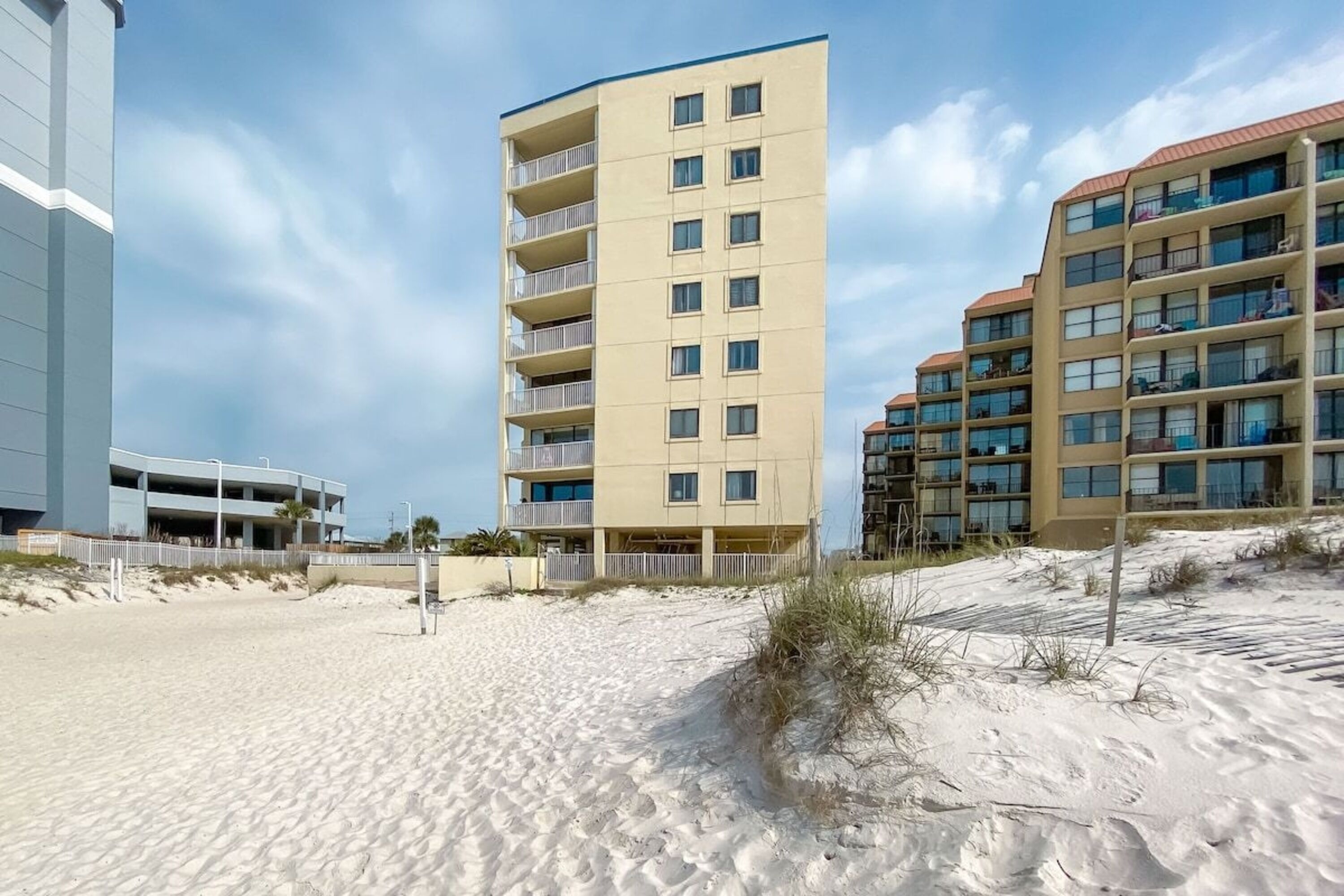 A beachfront hotel with multiple floors, balconies, and a sandy beach in the foreground.