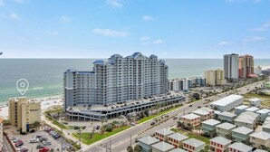 A high-rise hotel with multiple floors, a parking lot, and a view of the ocean. - The Whaler Condos (Gulf Shores)