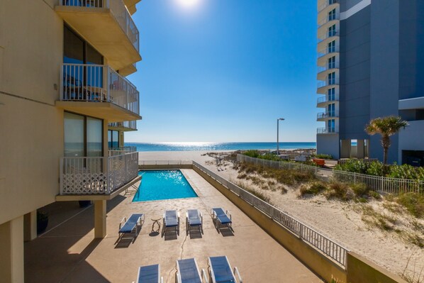 A pool area with lounge chairs and a view of the beach.