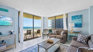 A living room with a sofa, coffee table, and a television on a wall. - The Whaler Condos (Gulf Shores)