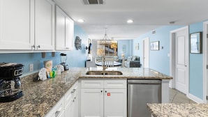 A kitchen with white cabinets, a granite countertop, a dishwasher, and a coffee maker. - The Whaler Condos (Gulf Shores)