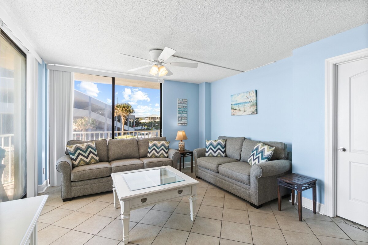 A living room with two sofas, a glass coffee table, and a ceiling fan.