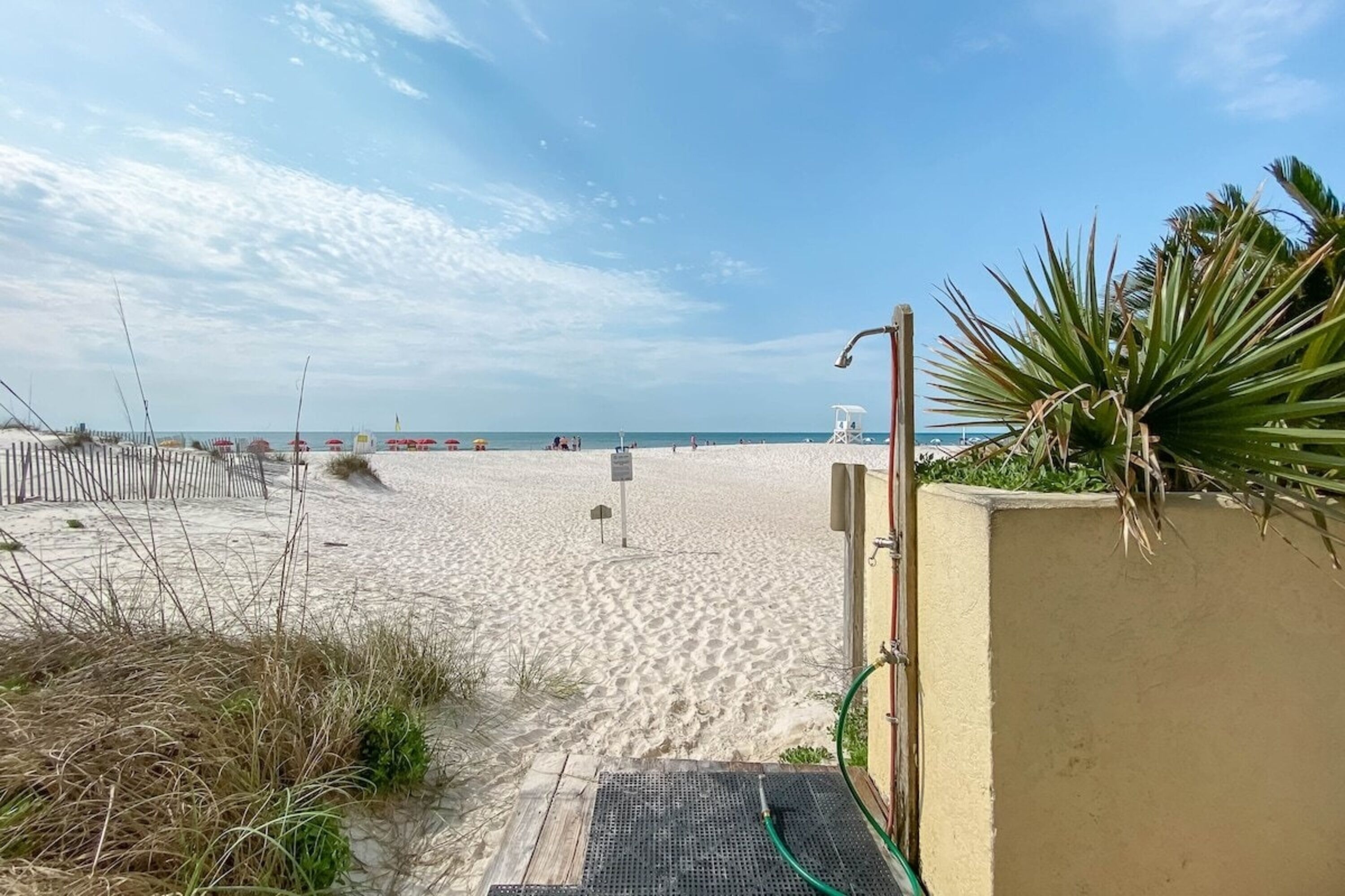 A sandy beach with a wooden fence, a lifeguard tower, and a palm plant.