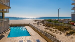 A swimming pool adjacent to a beach with a clear view of the ocean. - The Whaler Condos (Gulf Shores)
