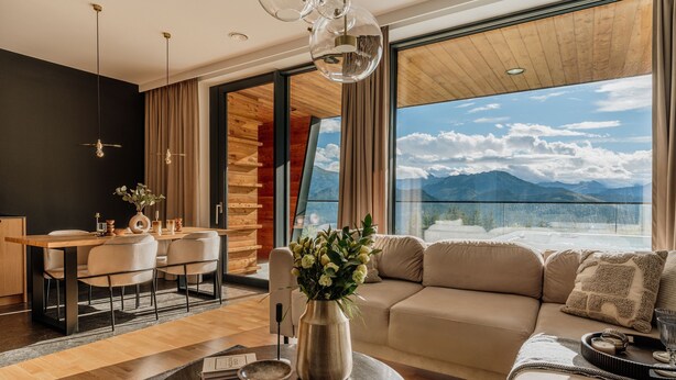A modern living room with a wooden dining table, a sofa, and a large window with a mountain view. - Salamandra Luxury Villas with Jacuzzi (Kościelisko)