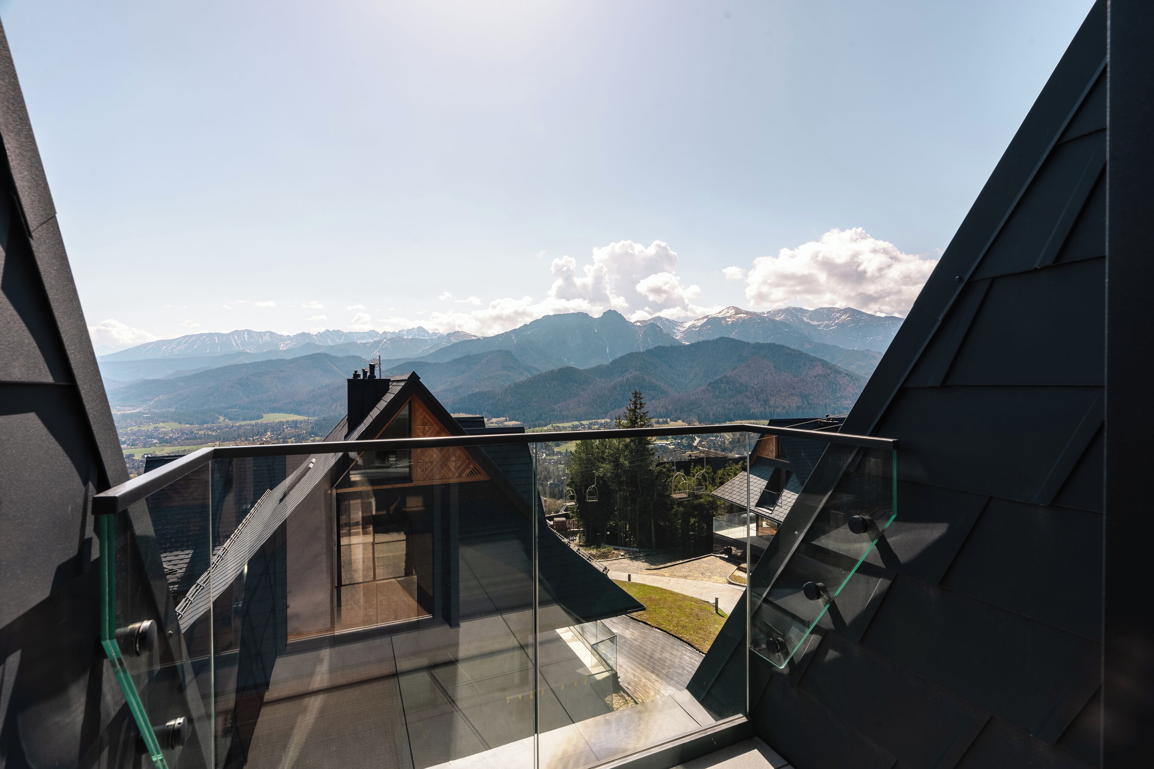 Un bâtiment moderne doté d’un balcon en verre offrant une vue sur un paysage montagneux.