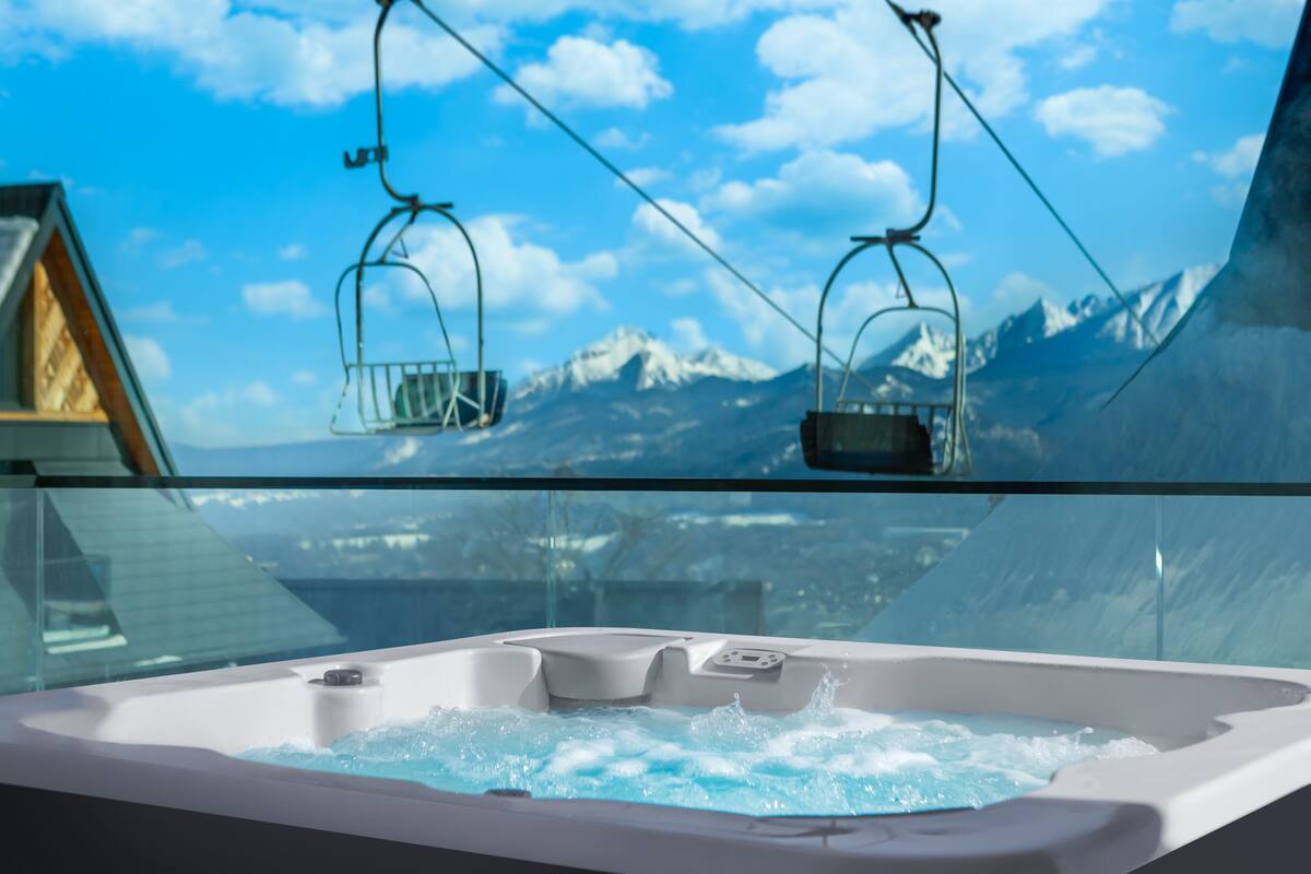 Un jacuzzi con vistas a la montaña, barandilla de cristal y un telesilla al fondo.