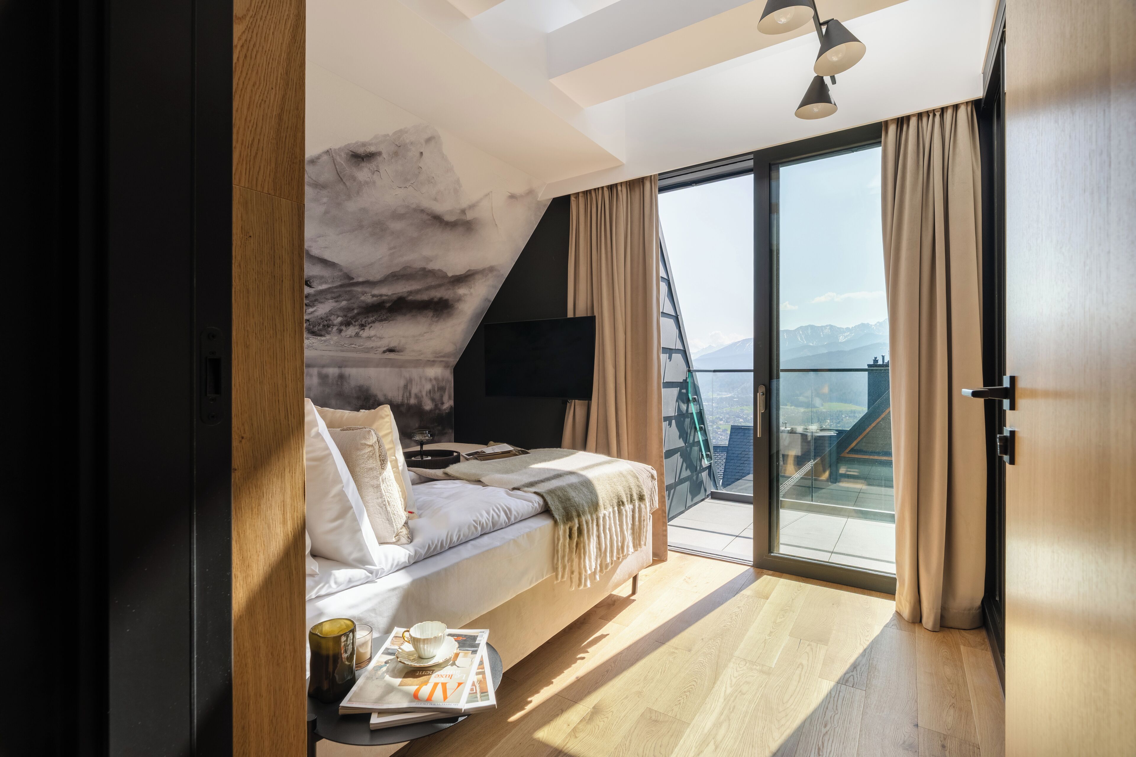 Une chambre à coucher moderne avec un lit, un téléviseur à écran plat, un magazine et une tasse posée sur une table d’appoint.