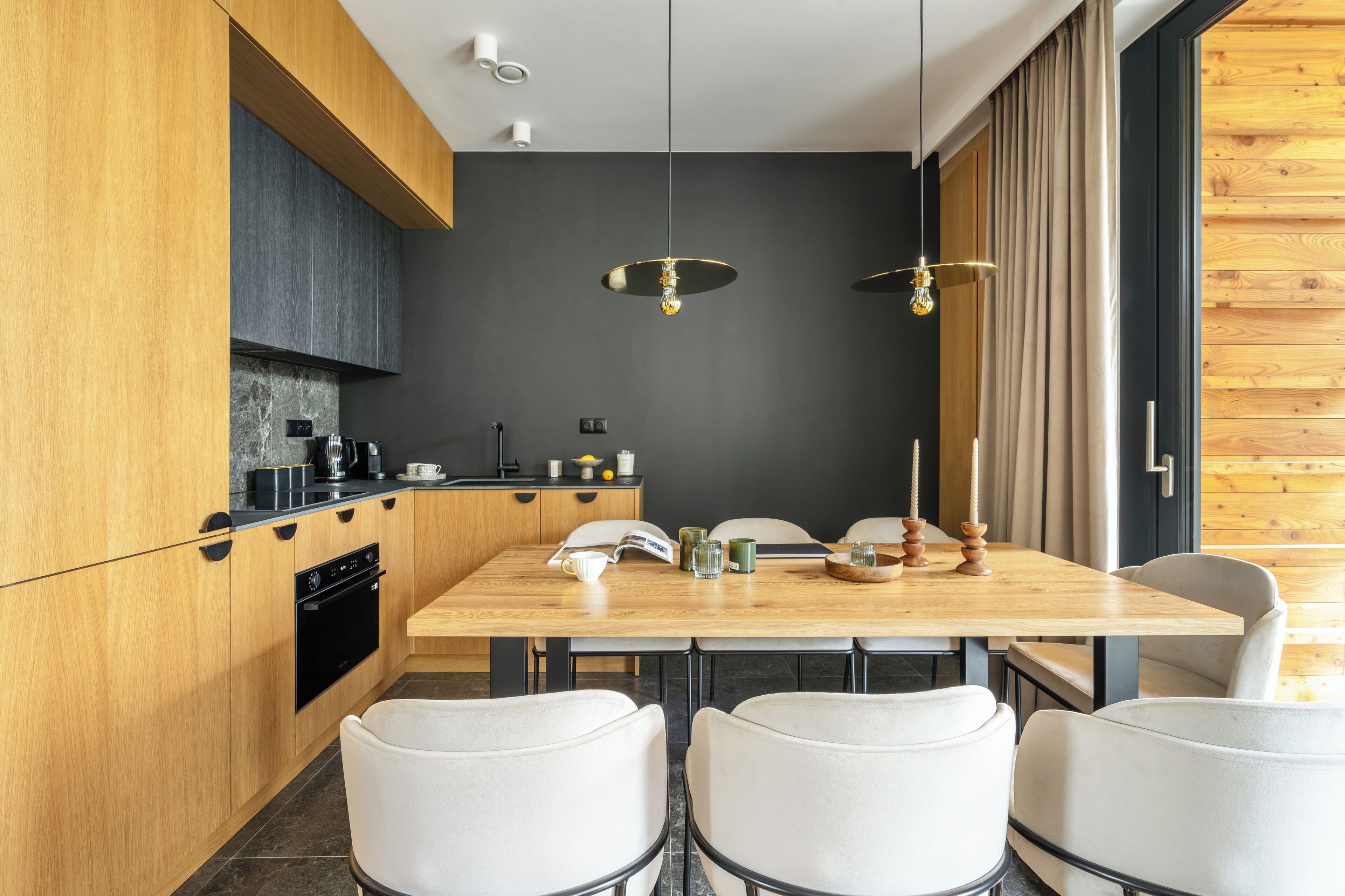 A modern kitchen with wooden cabinets, a black oven, and a dining area with a wooden table and white chairs.