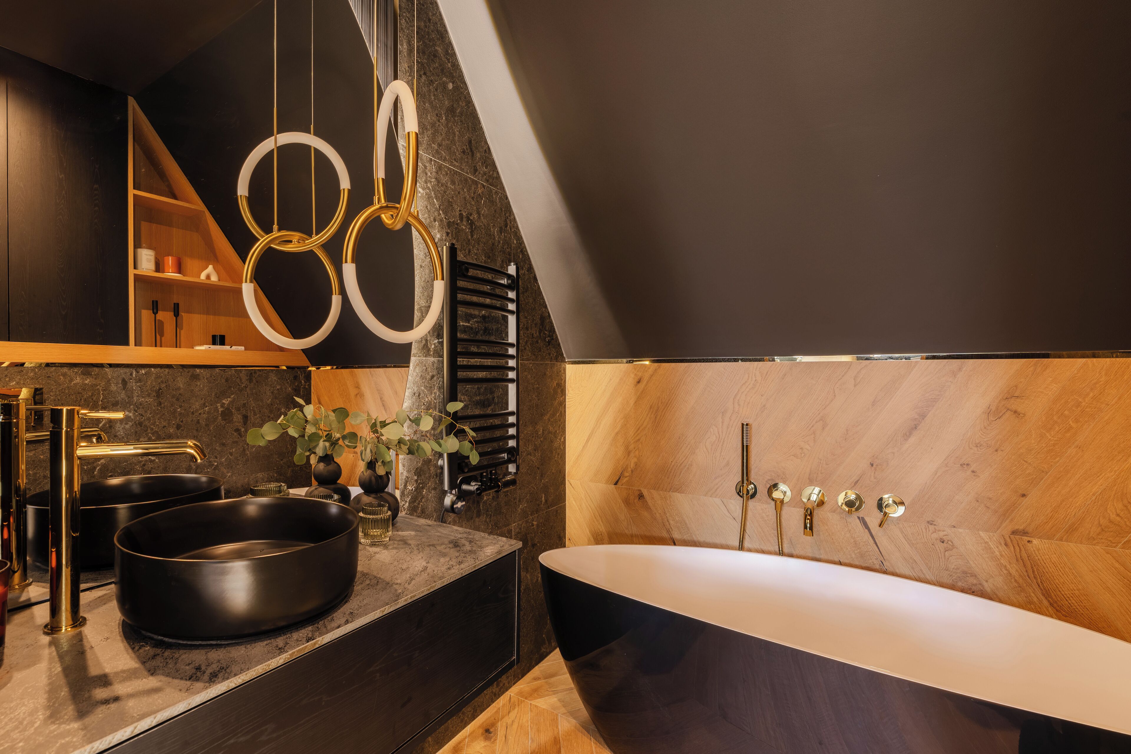 A modern bathroom with a freestanding bathtub, a vanity with black and gold fixtures, and a wooden shelf with toiletries.