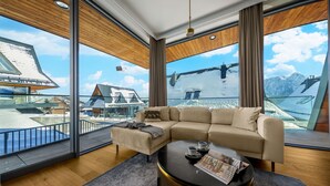 A modern living room with a large sectional sofa, a round coffee table, and a view of a snowy mountain landscape through large windows. - Salamandra Luxury Villas with Jacuzzi (Kościelisko)