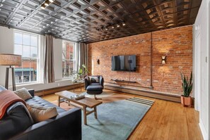 Una sala moderna con pared de ladrillo, televisor de pantalla plana, sofá de cuero, mesa de centro de madera y un ventanal grande.