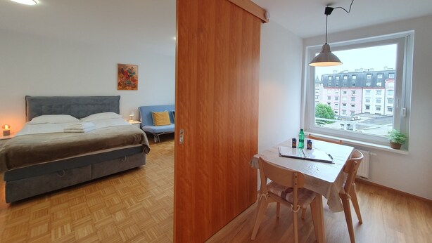 Un dormitorio moderno con cama, mesita de noche y ventana con vistas a edificios.