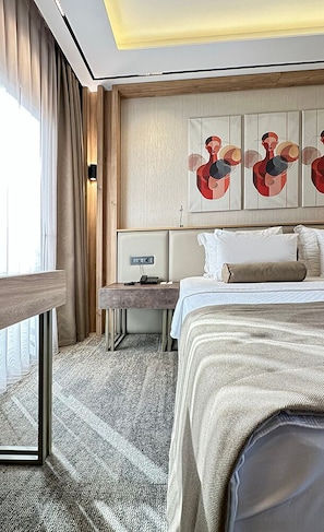 A hotel room with a bed, bedside table, lamp, artwork, and a view of the outdoors.