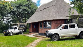 A thatched-roof building with a brick exterior, a covered outdoor seating area, and two white pickup trucks parked in front.