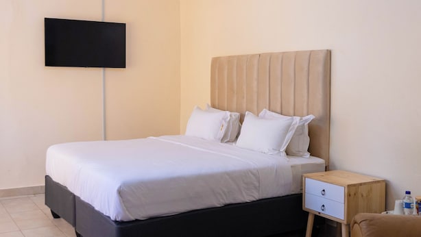 A neatly arranged bedroom with a bed, bedside table, and a TV mounted on the wall. - Spring Resort  (Hurungwe)