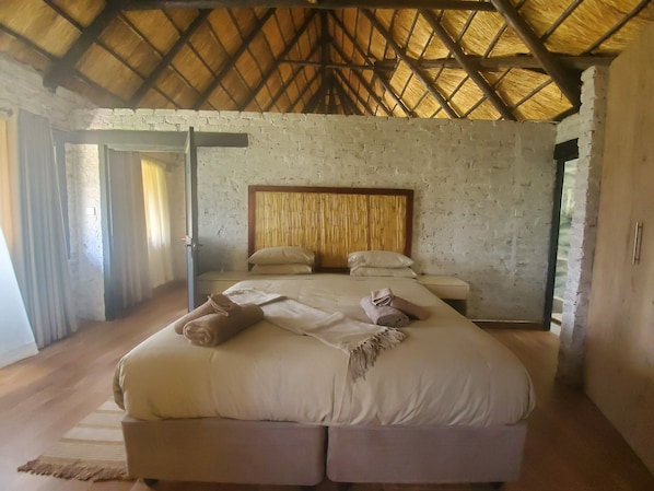 A spacious bedroom with a large bed, a wooden headboard, and a thatched roof ceiling.