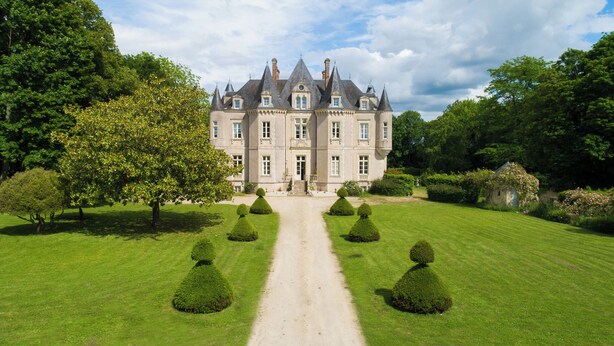 Un grand bâtiment historique à la façade symétrique, doté d’une entrée centrale et d’un jardin bien entretenu, avec un chemin de gravier menant à l’entrée.