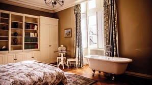 Une chambre à coucher avec un grand lit, une armoire blanche, une petite table avec des chaises, une baignoire et une fenêtre avec des rideaux.