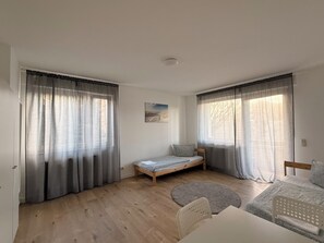 Una habitación con cama, una mesita, una silla y un ventanal con cortinas.