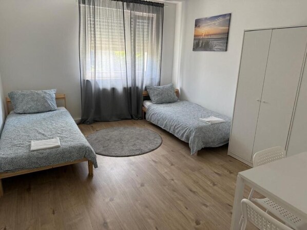 A room with two single beds, a round rug, a white wardrobe, and a painting on the wall.