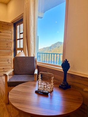 A wooden interior with a round table, a chair, a remote control, and a decorative item. - Oakridge By The Aravali Story (Dhanaulti)