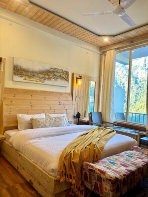 A bedroom with a large bed, a wooden headboard, a painting, a desk, and a view of the outdoors.