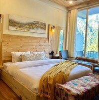 Una cama de madera con ropa de cama blanca, vistas a árboles a través de una ventana y un cuadro en la pared.