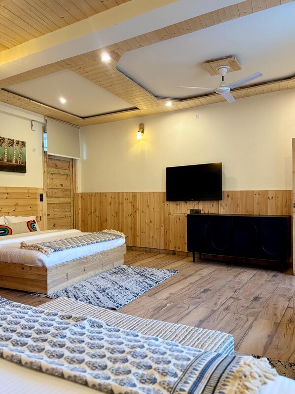 A bedroom with a bed, a television, a ceiling fan, and wooden panel walls. - Oakridge By The Aravali Story (Dhanaulti)